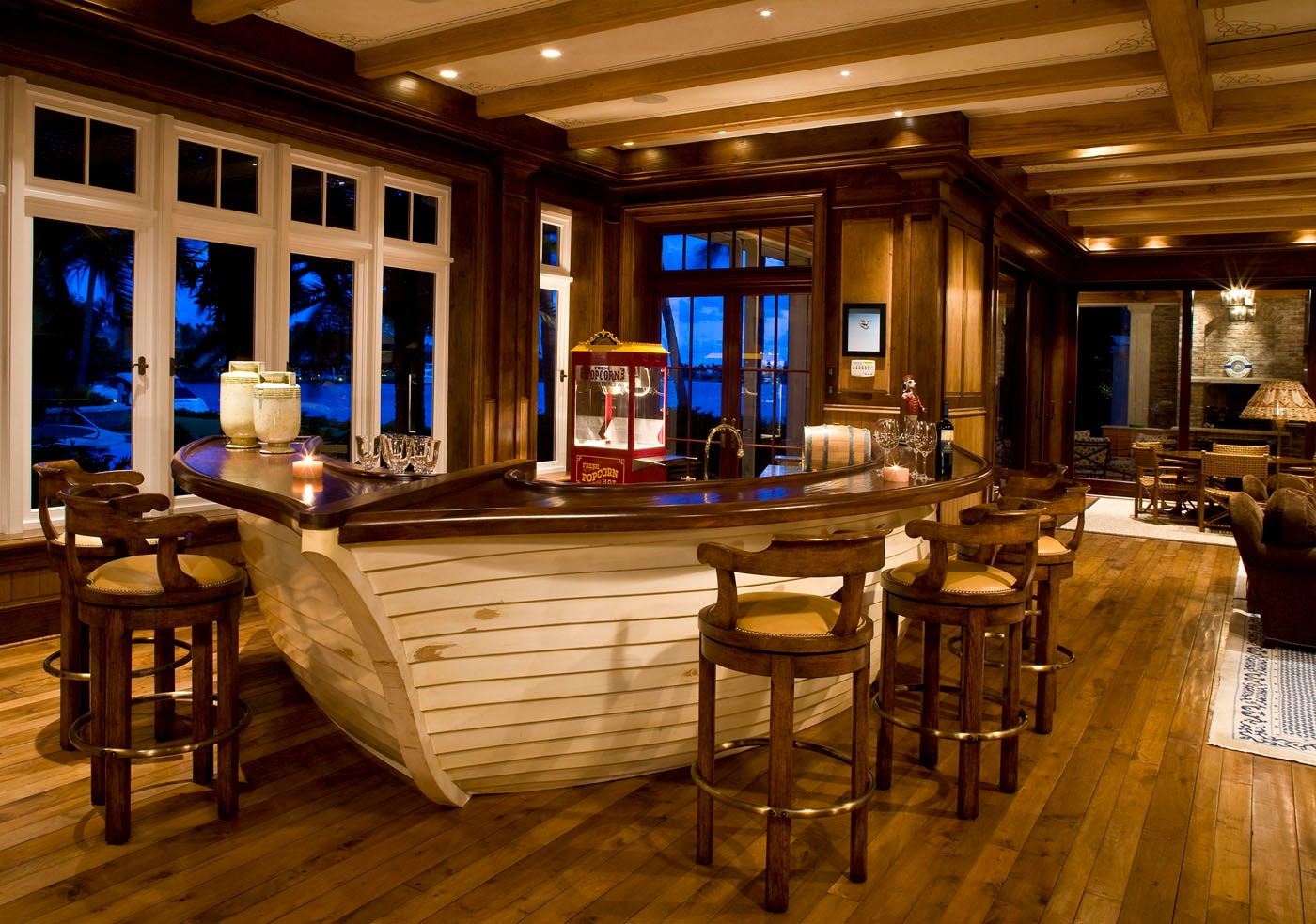 Nautical-themed bar built from a boat hull with coffered wood ceiling and waterfront view at night