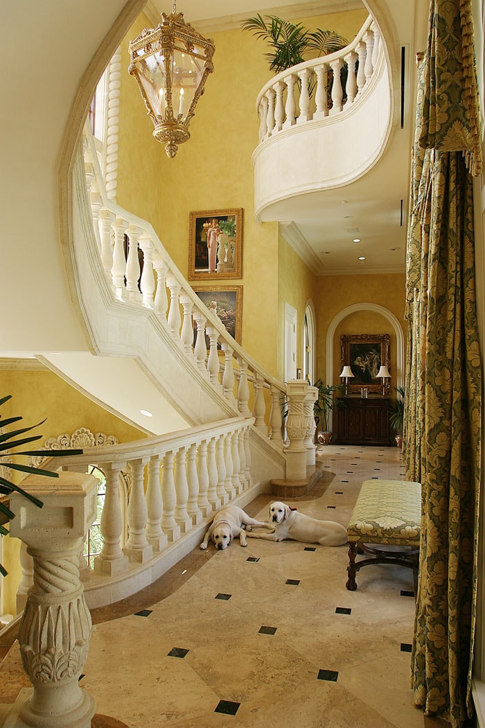 Grand curved staircase foyer with yellow walls, marble floors and two yellow Labrador Retrievers