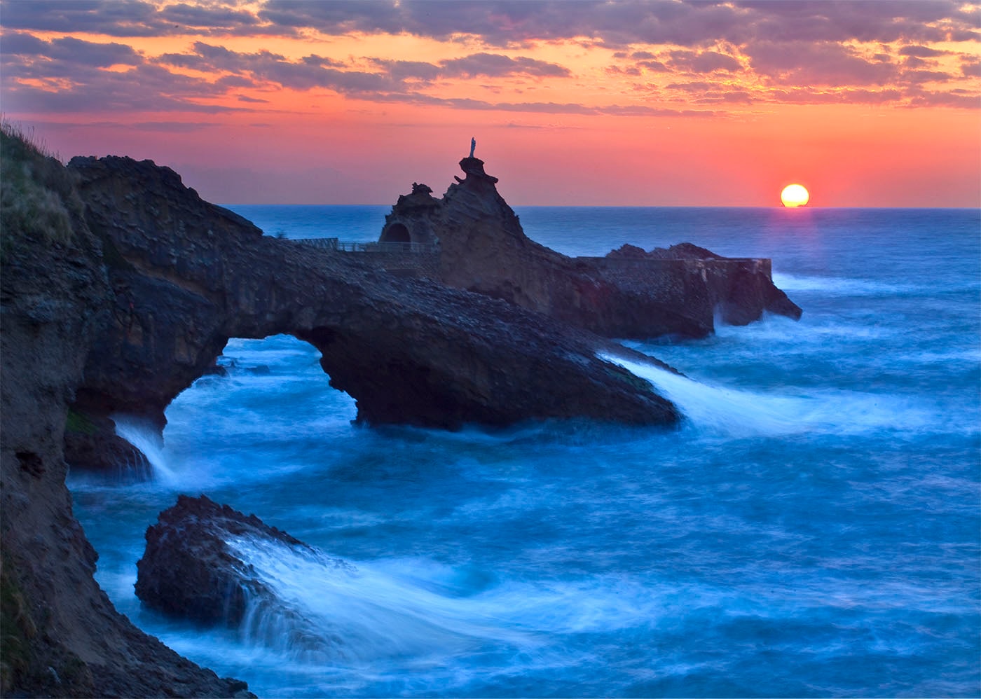 Dramatic coastal sunset over rocky sea arch with long-exposure waves